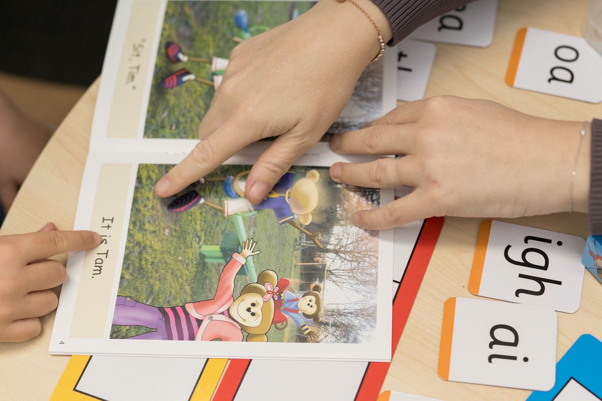 A speech pathologist guiding a child through sound-tapping with letter tiles, both leaning in as the child sounds out a word
